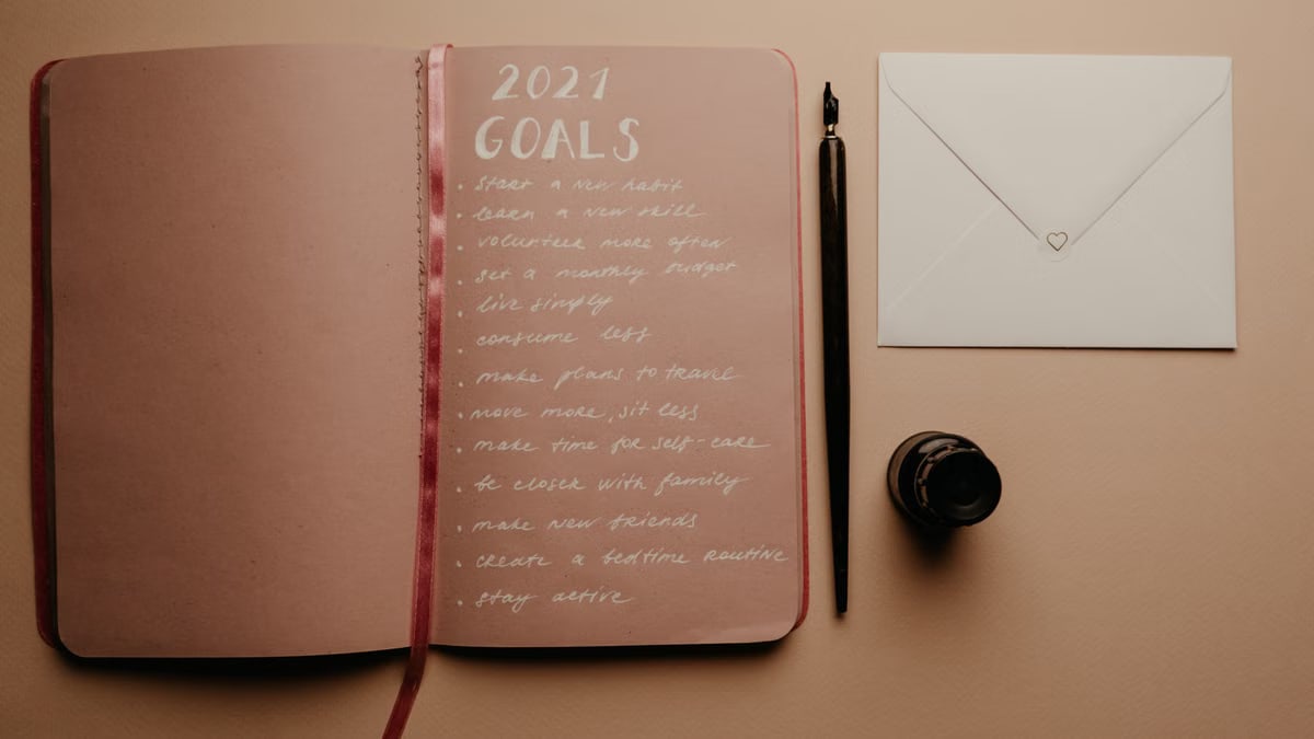 Open notebook with 2021 goals, calligraphy pen, envelope, and ink jar on neutral background.